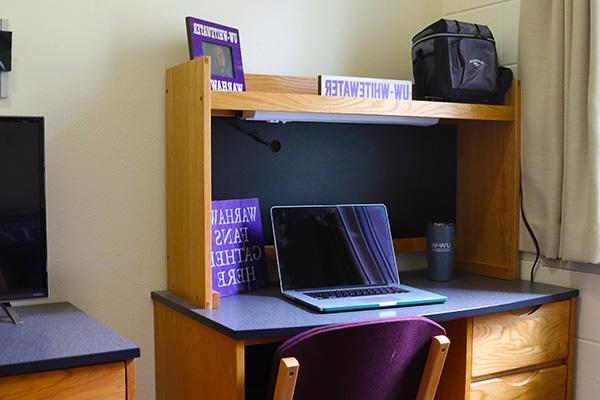 A desk. There is a laptop, a picture and a water bottle on top of the desk.