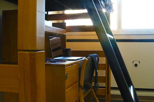 Underneath a lofted bed, there is a desk with a laptop on top of it.